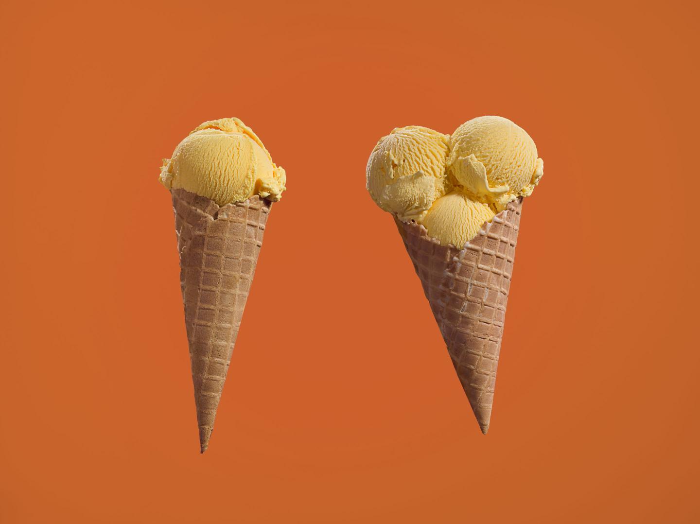 Two ice cream cones, one on the left with one scoop and one on the right with three scoops.