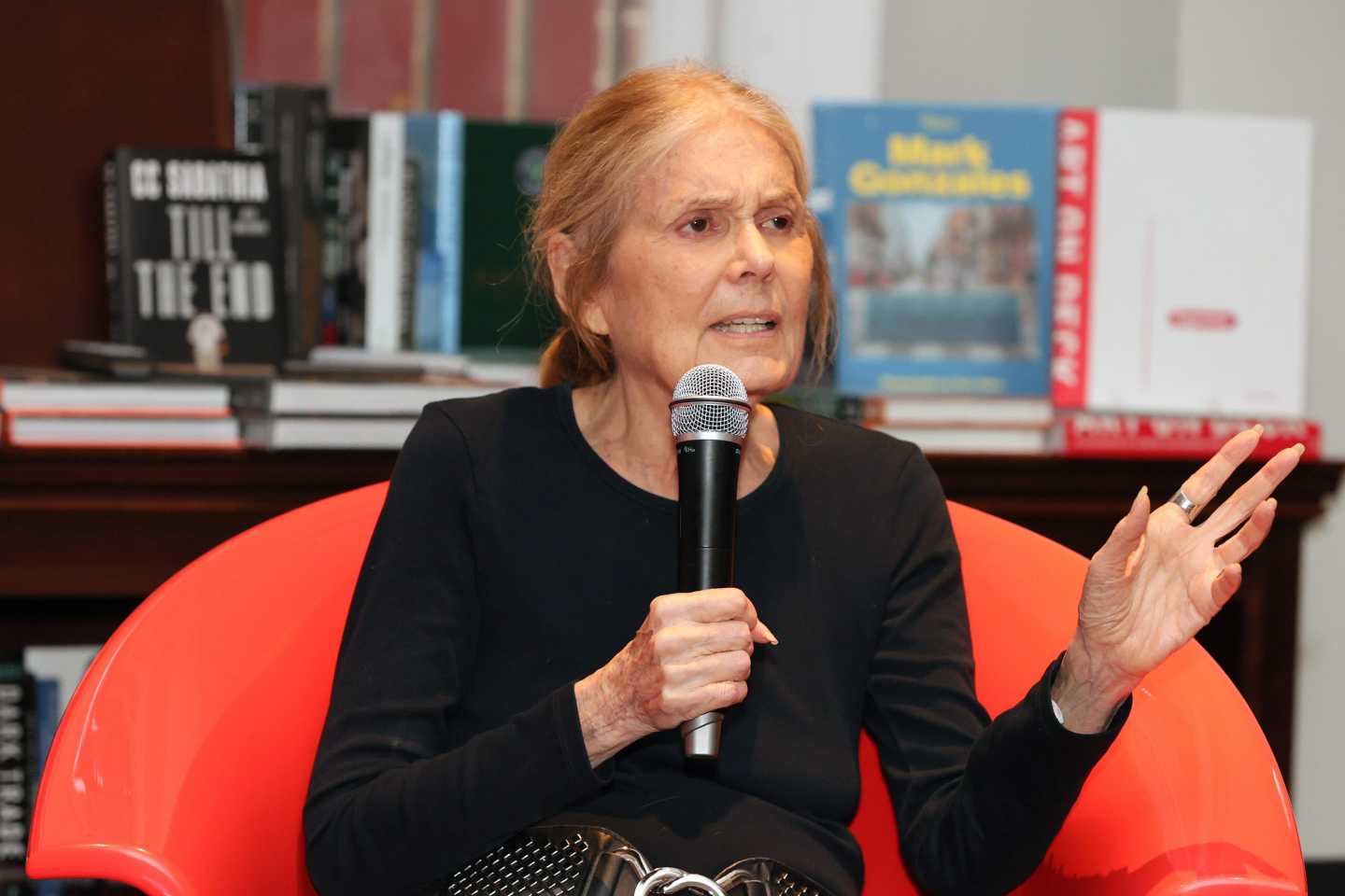 Gloria Steinem sitting in a red chair with a hand-held microphone