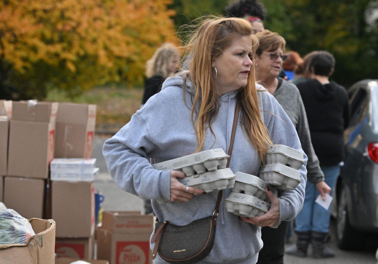 A woman in a grey hoodie holds six cartons of eggs in her arms.