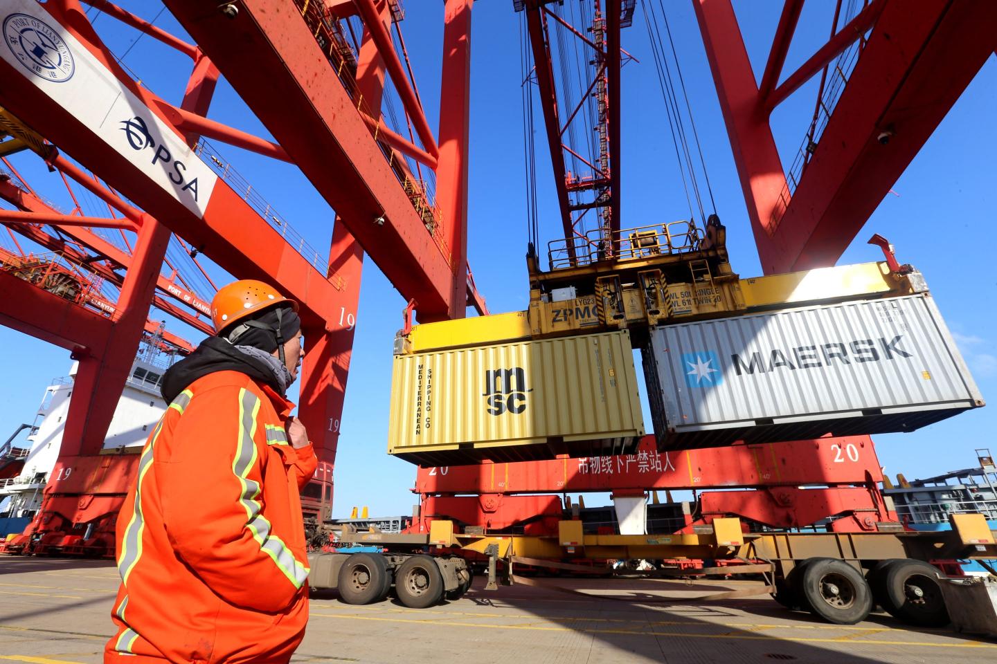 A dock workers watching a crane hoist up shipping containers.