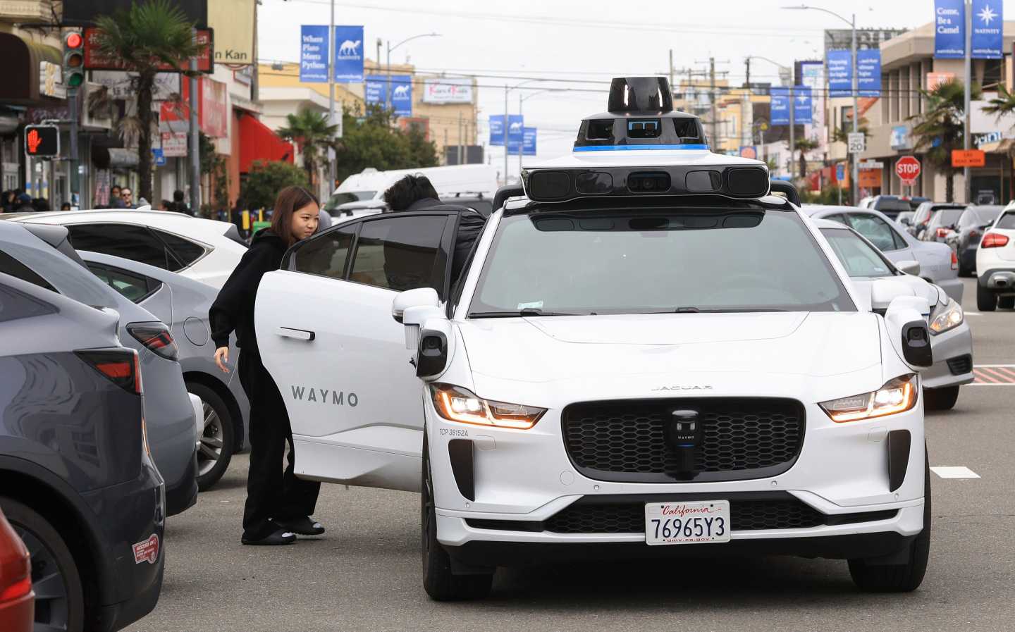 A woman gets out of a white Waymo van.
