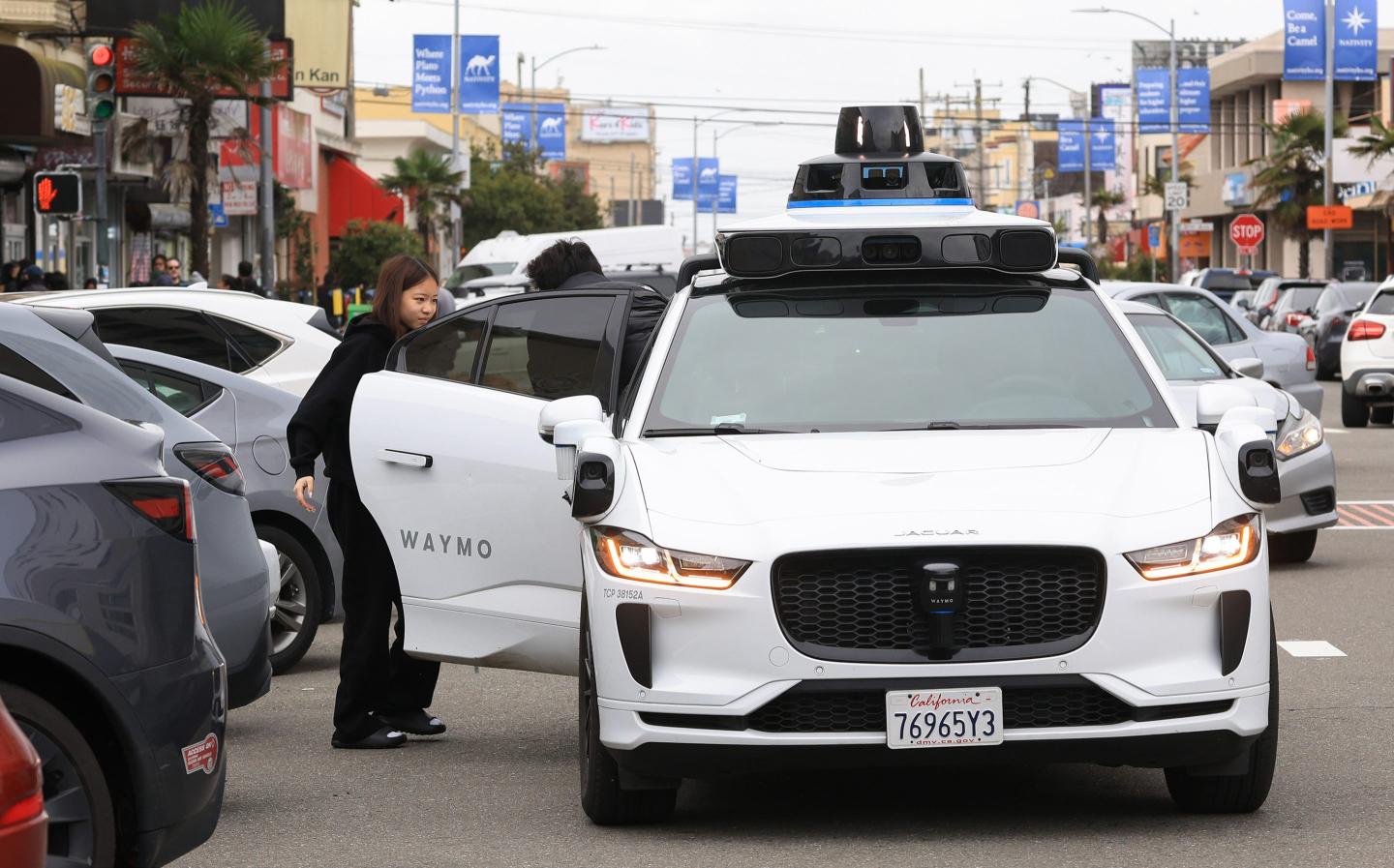 A woman gets out of a white Waymo van.