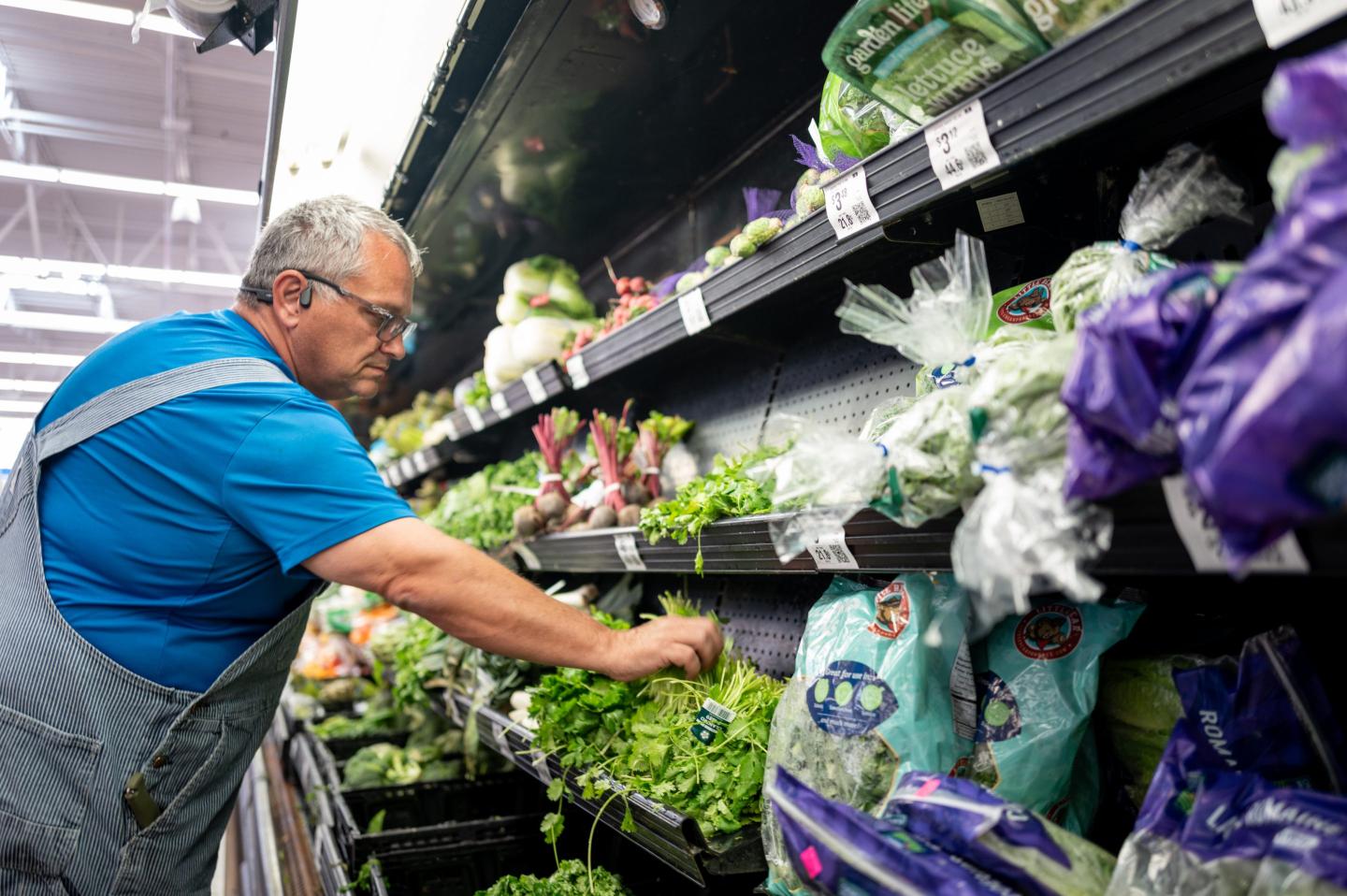 A man looks at herbs in the produce aisle of a grocery store.