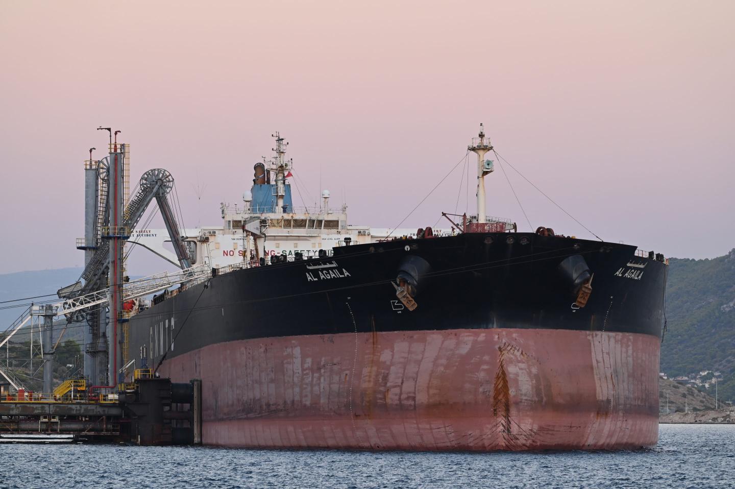 An oil tanker on the water in front of a setting sun.