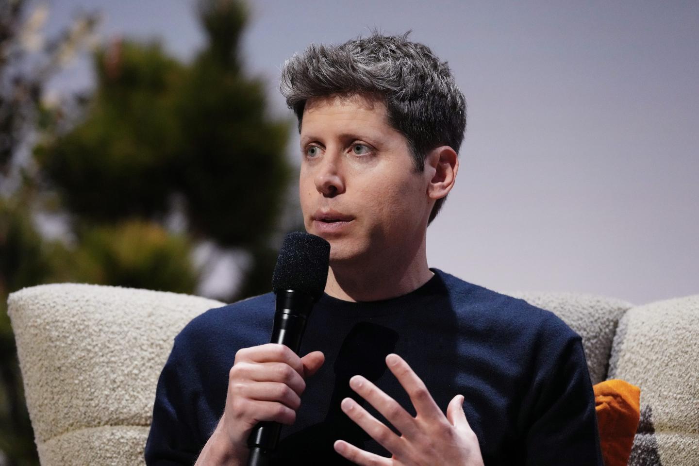 Sam Altman, sitting and holding a microphone to his mouth