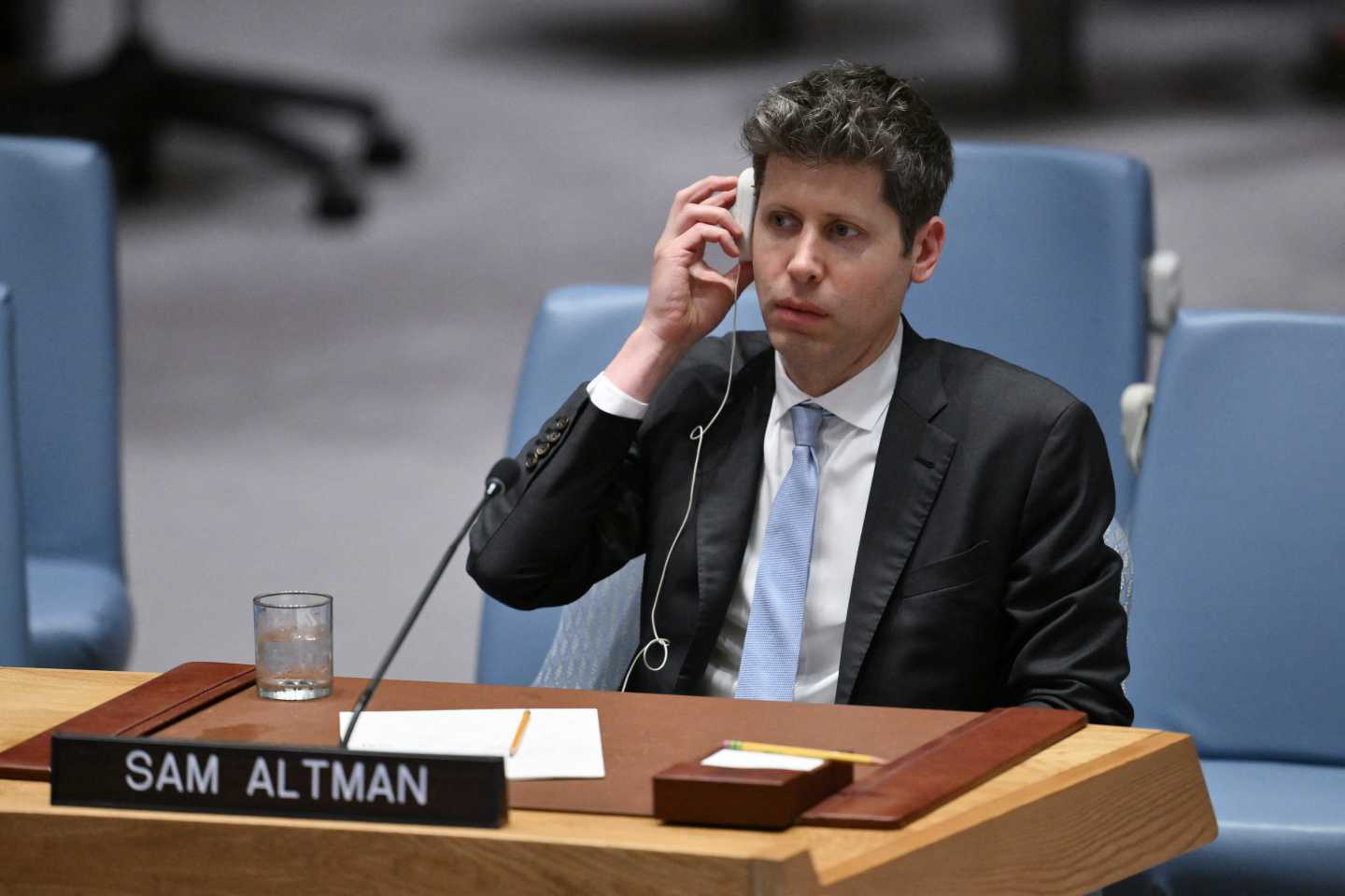 OpenAI CEO Sam Altman sitting at a table while appearing before the UN Security Council and holding an earphone to one ear.