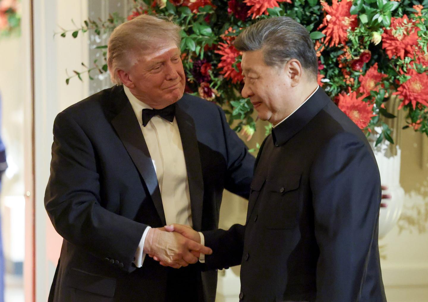 Donald Trump and Xi Jinping, both wearing tuxedoes, shake hands.