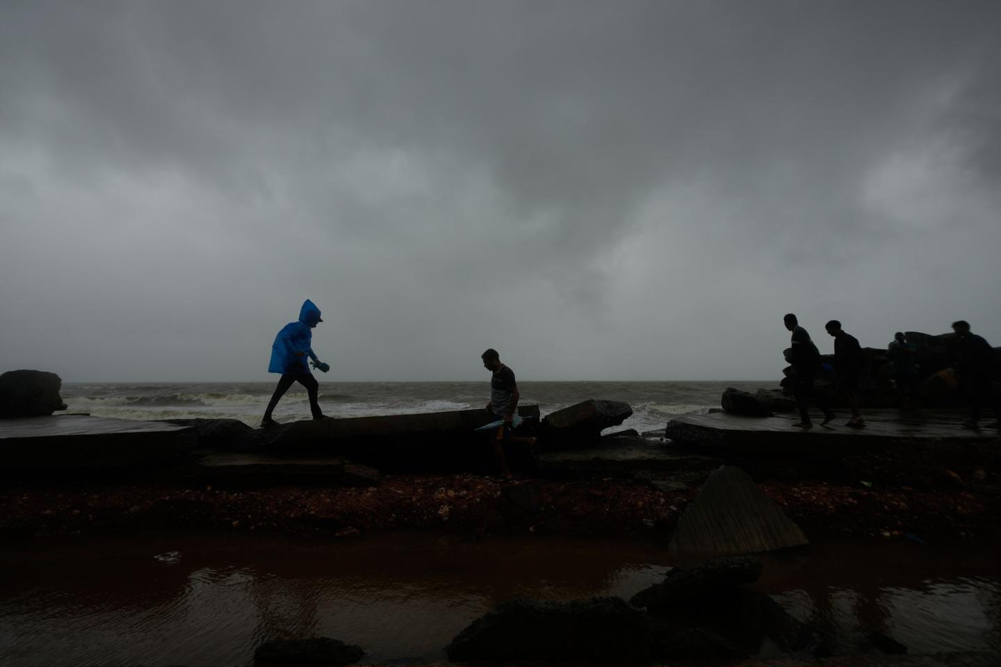 People walk on a damaged road near the shore in Uppada, Kakinada, India