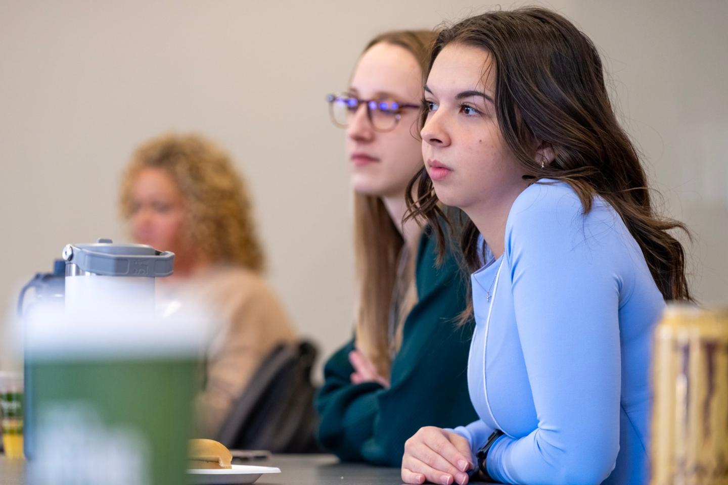 Ella Traina, right, wears a blue shirt while sitting at a table looking off camera