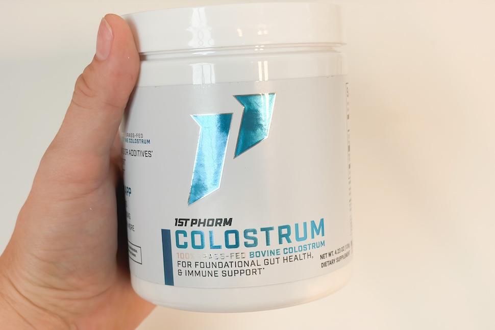 Closeup of a hand holding a canister of 1st Phorm Colostrum