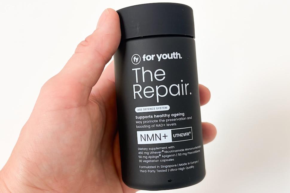 Closeup of a hand holding a black bottle of For Youth The Repair NMN+