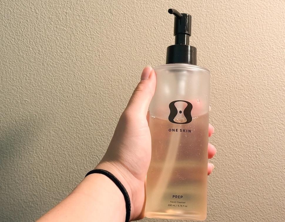 Closeup of a hand holding a bottle of One Skin Prep Facial Cleanser