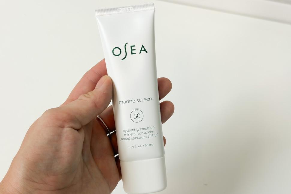 Closeup of a hand holding a tube of OSEA Marine Screen SPF 50 Mineral Sunscreen