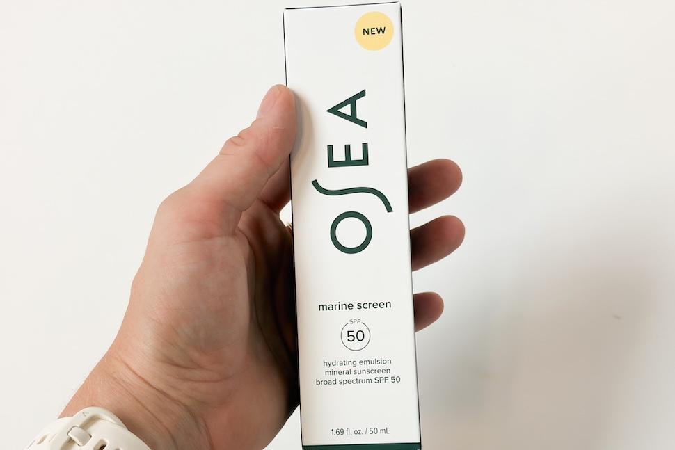 Closeup of a hand holding OSEA Marine Screen SPF 50 Mineral Sunscreen, still in its box