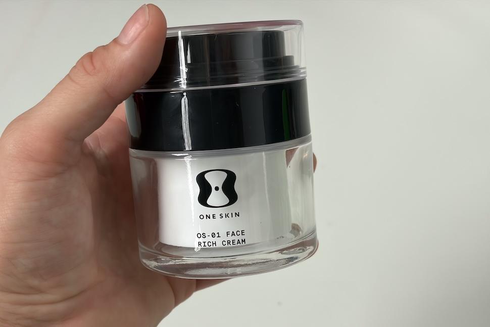 Closeup of a hand holding a jar of OneSkin Face Rich Cream