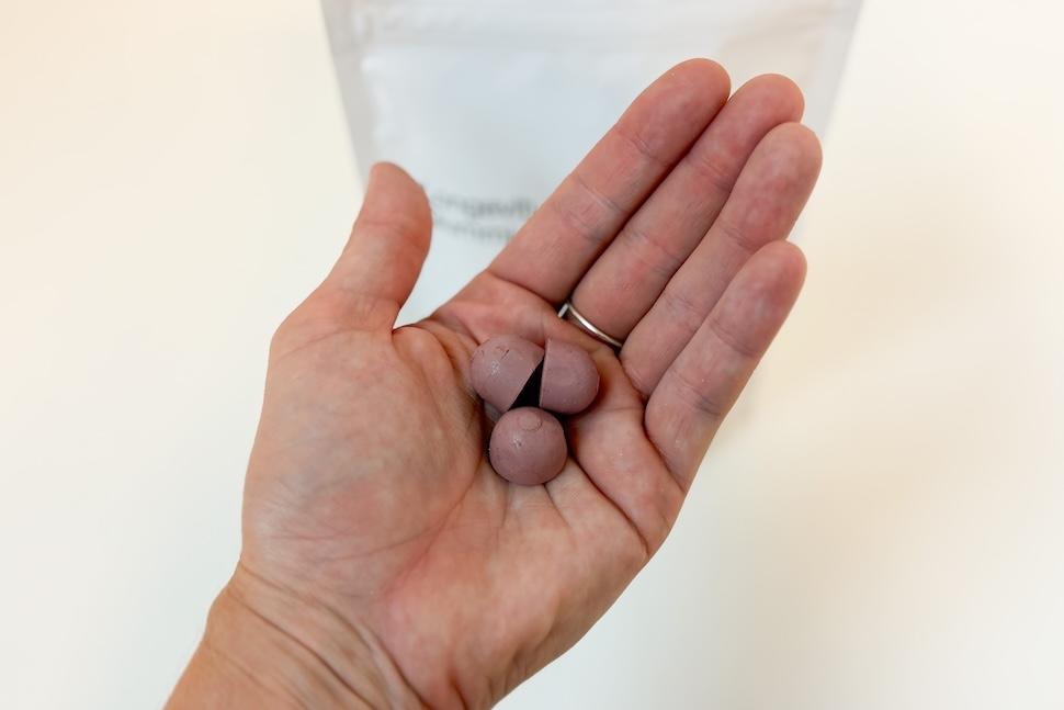 Closeup of a hand holding three Timeline Mitopure Gummies. The gummies are a light purple color, and you can see the white bag of them on the countertop below.