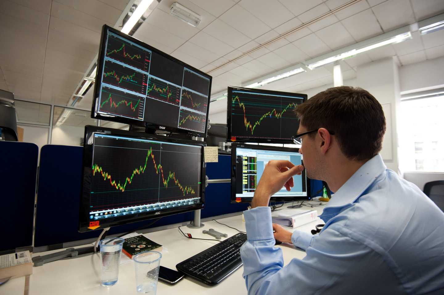 A man looks at several stock trading charts on four computer displays.