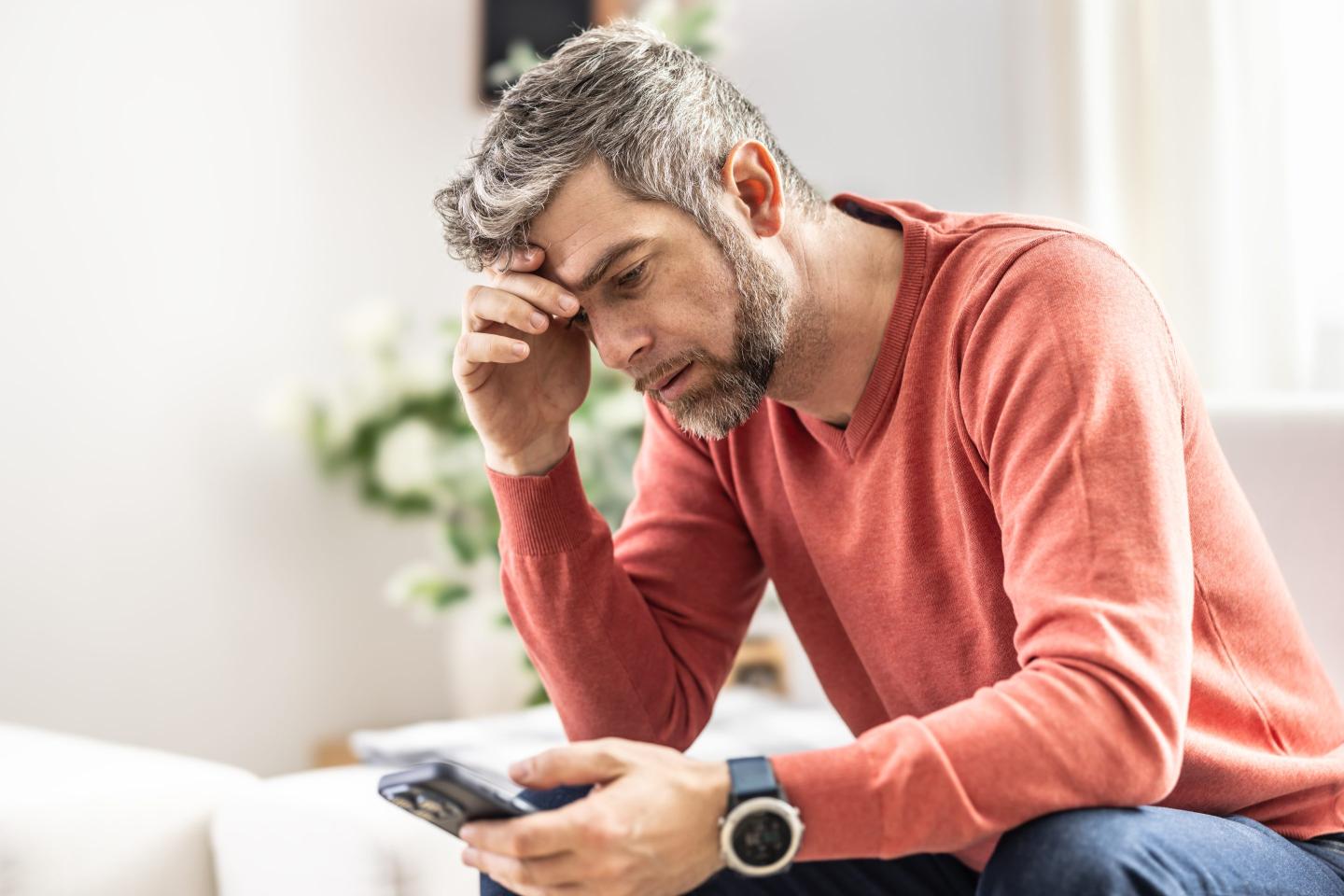 A man sits with his head in his hand, frowning at his phone.