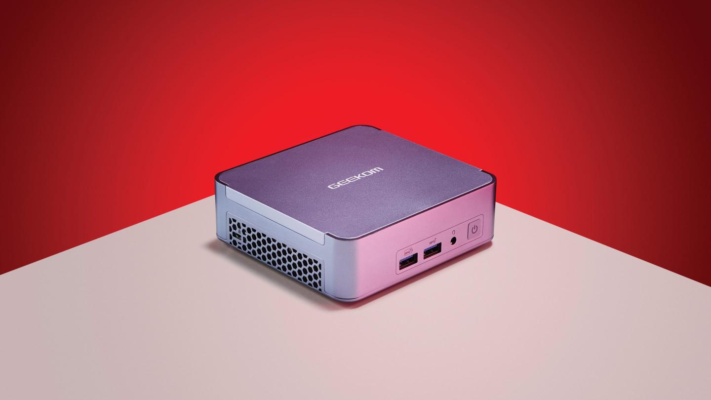 A Geekom Mini PC sitting on a white table against a red background.
