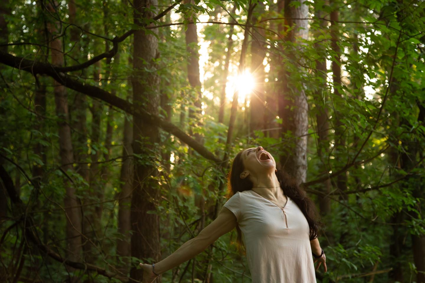 Beauty woman joyfully shouting in the forest in summer day. Magic natural light in a pine park among the trees.