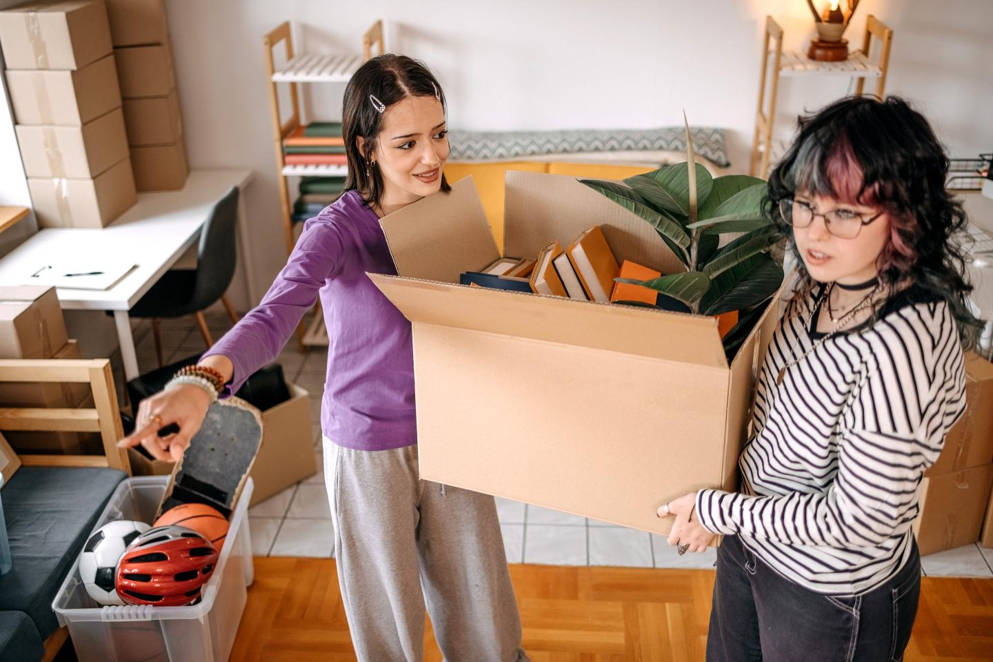 Two young people hold moving boxes in an apartment