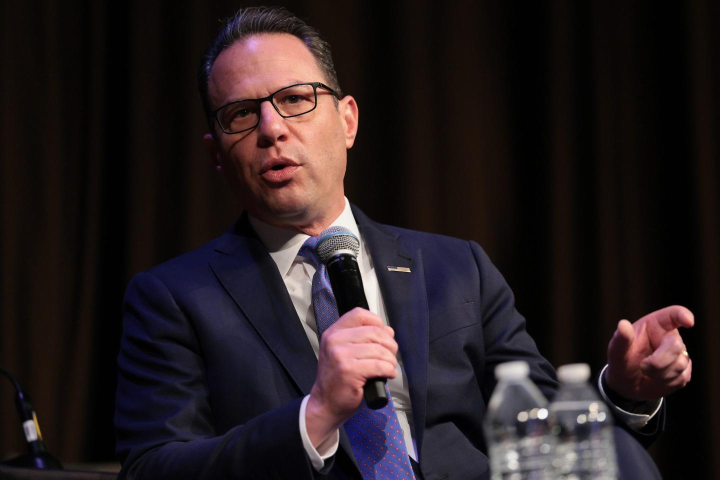 Josh Shapiro, wearing a suit, speaks into a microphone.