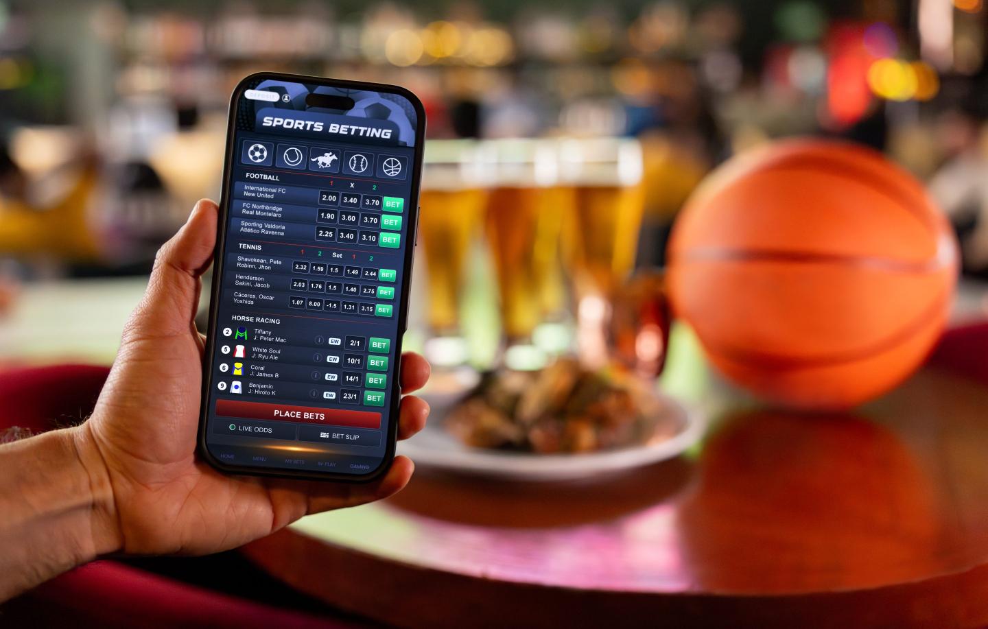 Person holds up phone showing sports betting stats with a basketball and beers in the background.