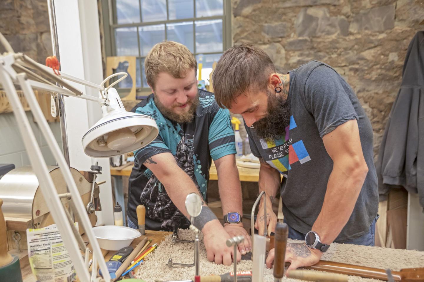 Two men operate a machine to string guitars.