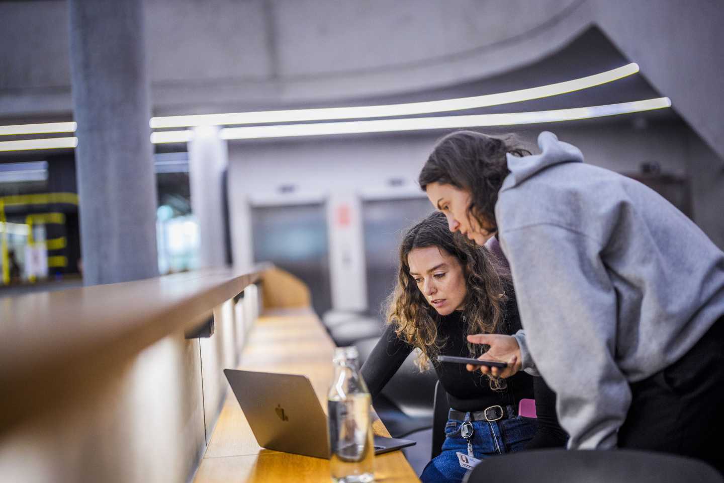 Photo of two young women hunching over laptop