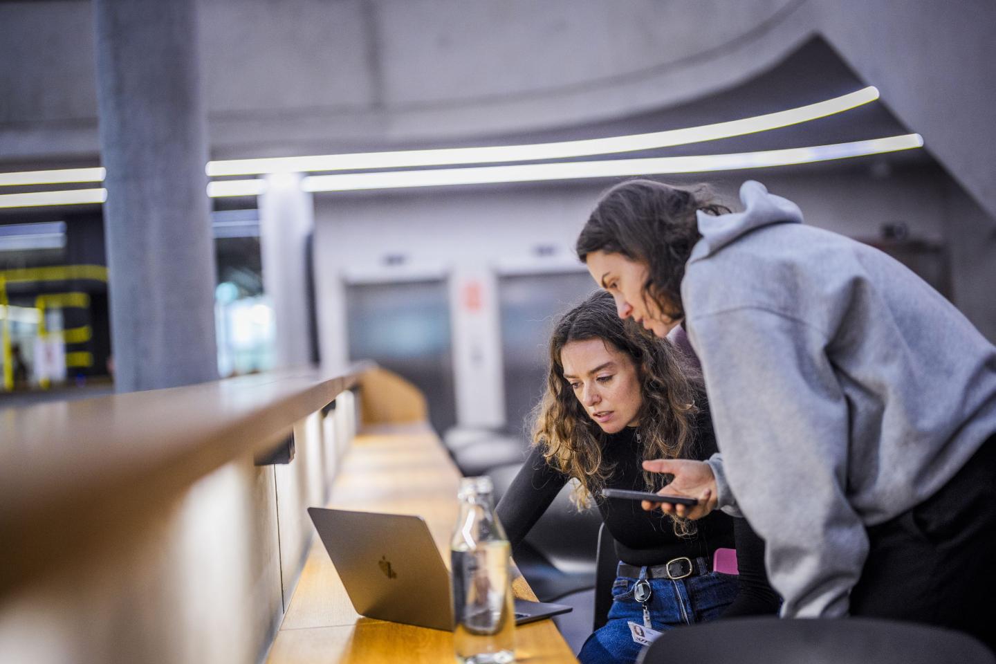 Photo of two young women hunching over laptop