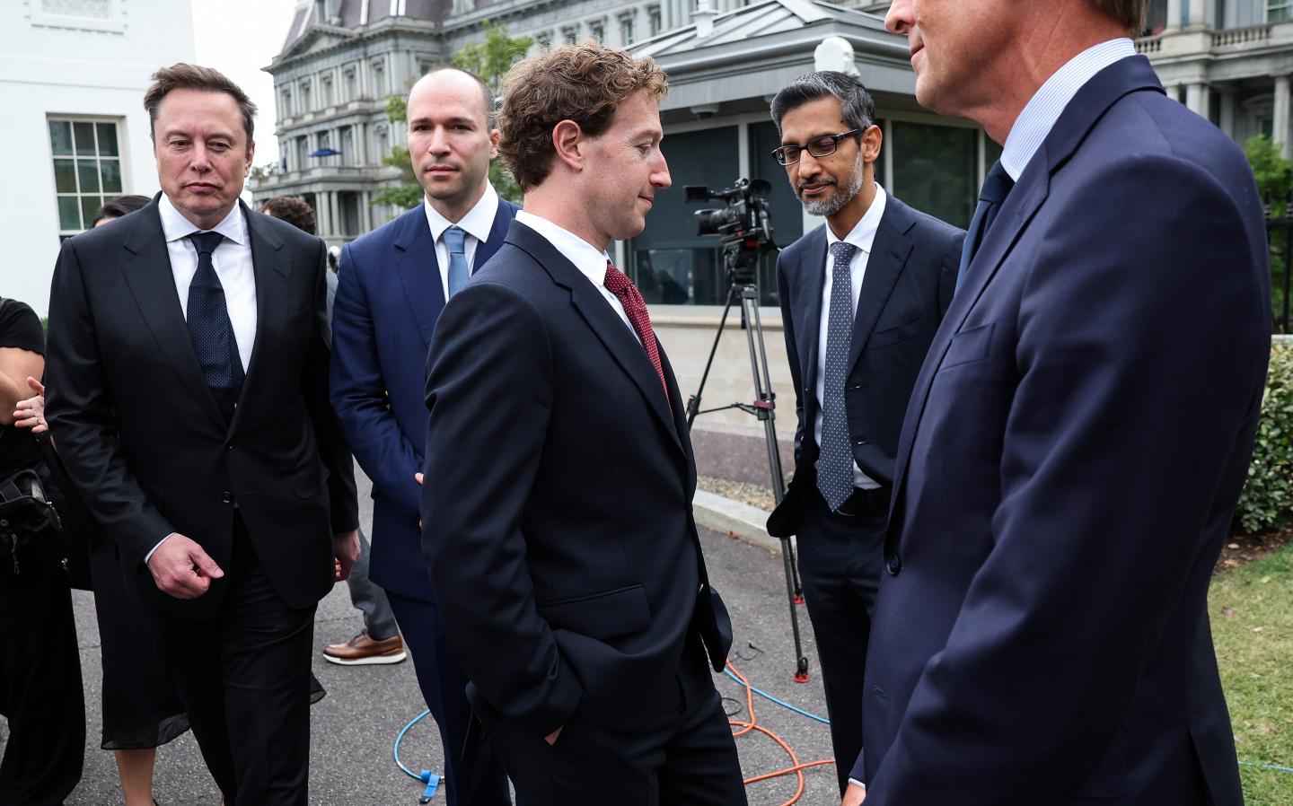 A group of men including Elon Musk, Mark Zuckerberg, and Sundar Pichai, stand around in front of the West Wing of the White House.