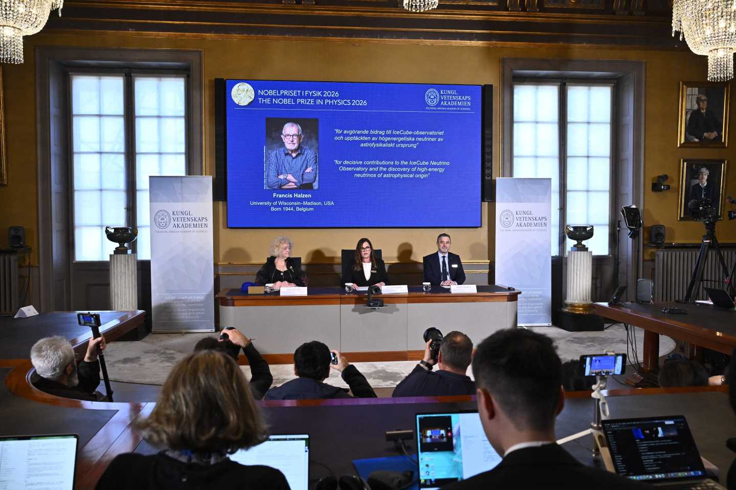 Eva Olsson, Ellen Moons, and Mark Pearce sit in front of a screen displaying Francis Halzen as the recipient of the 2026 Nobel Prize in Physics during a press conference at the Royal Swedish Academy of Sciences in Stockholm, Sweden, on October 6, 2026. Belgian physicist Francis Halzen won the Nobel Prize in Physics for work on subatomic particles at the South Pole, the Nobel jury said.