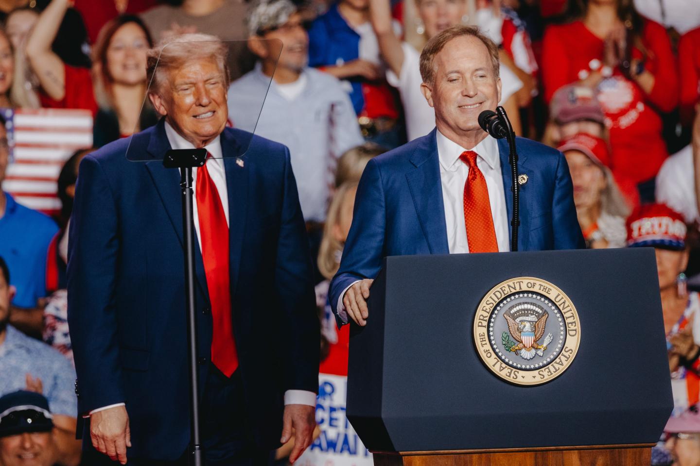 Ken Paxton stands behind a podium and Donald Trump stands next to him.