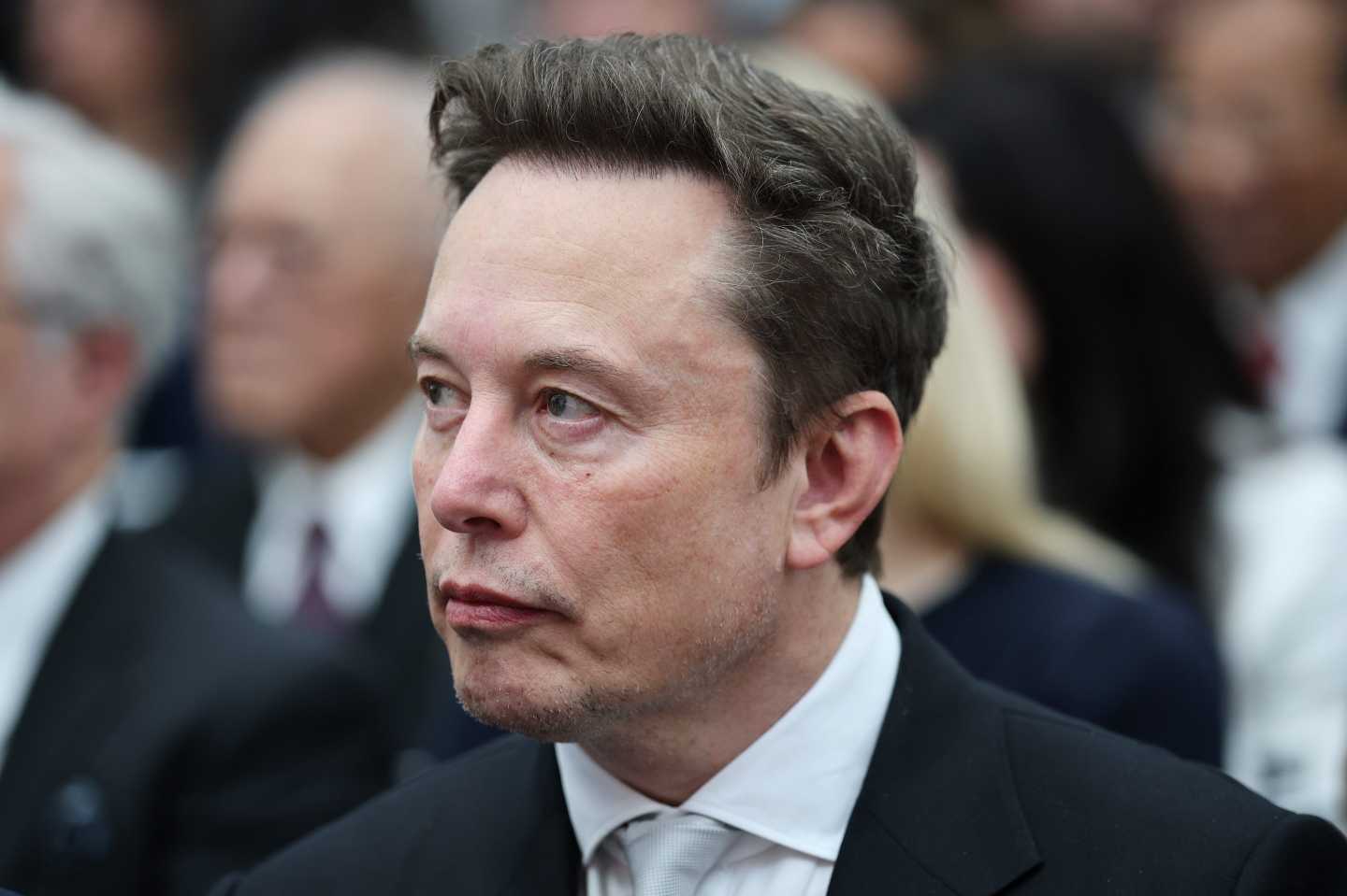 Elon Musk, wearing a suit, frowns and looks to his right.