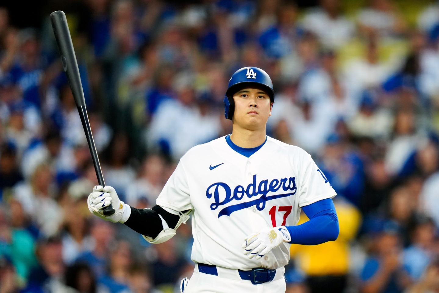 Shohei Ohtani frowns as he holds a baseball bat up with one arm.