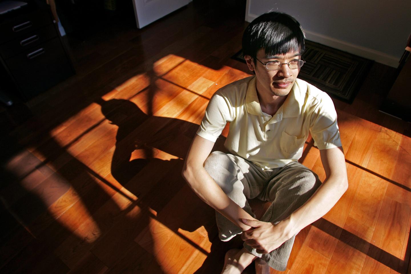 Photo of mathematician Terence Tao sitting cross-legged on a wood floor, partly in sun and partly in shadow, shot from above.