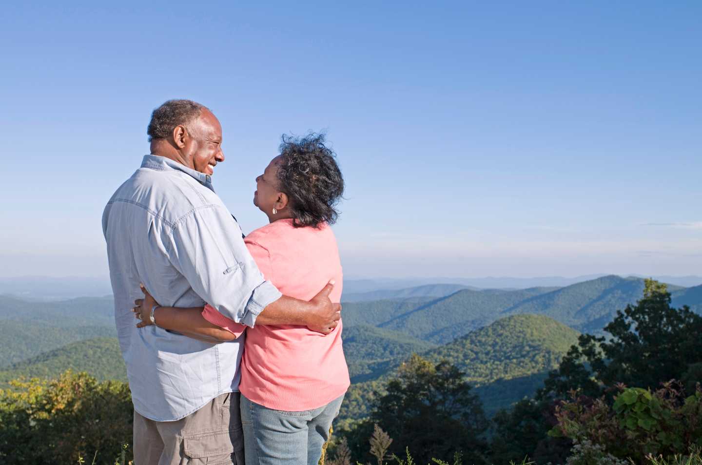 Senior couple embracing on hill, smiling at each other