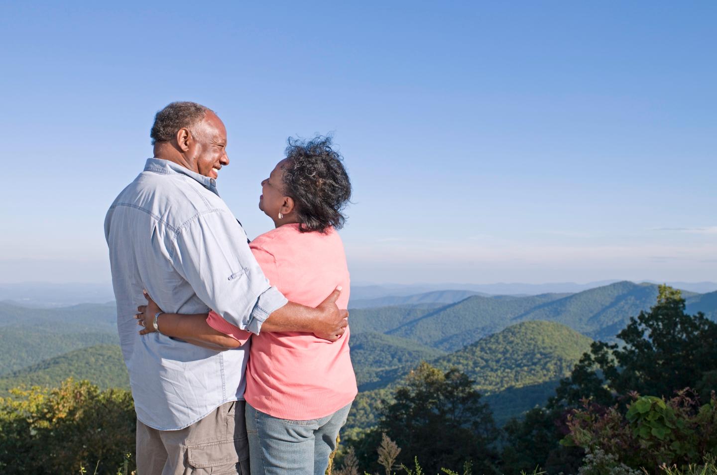 Senior couple embracing on hill, smiling at each other