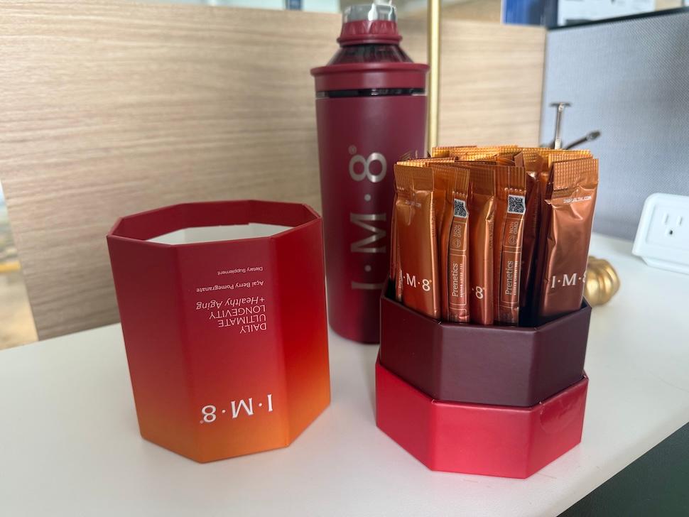 An IM8 kit on a bathroom countertop. The container is open, showing all of the individual powder packets inside. You can also see the shaker bottle in the background.