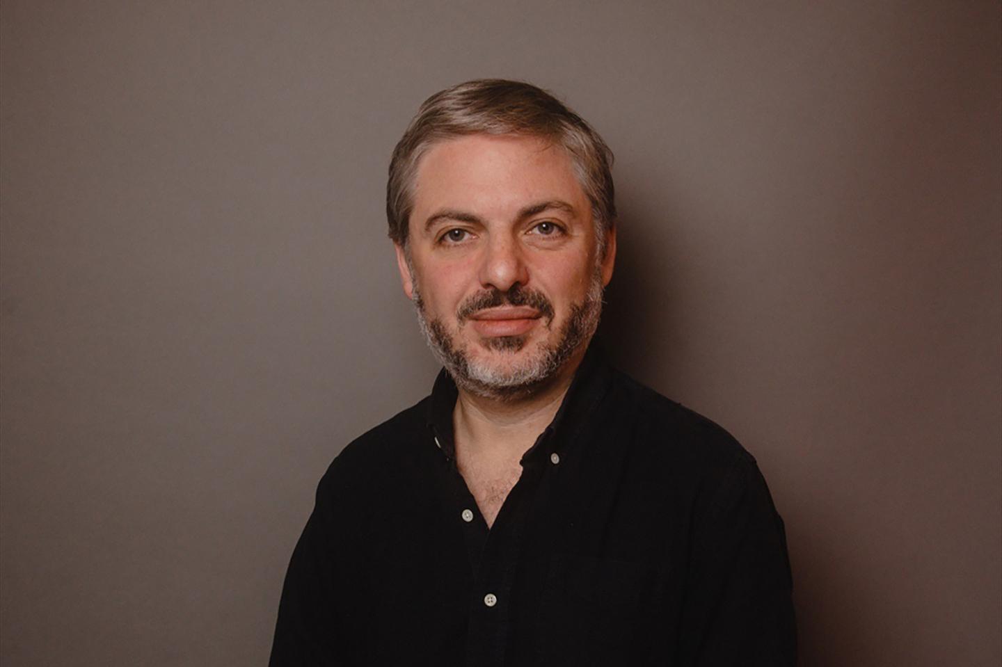 Daniel Simon smiles for a headshot wearing a black button up.
