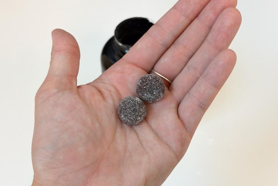 Closeup of an open palm holding two dark purple Legion Magnesium Gummies
