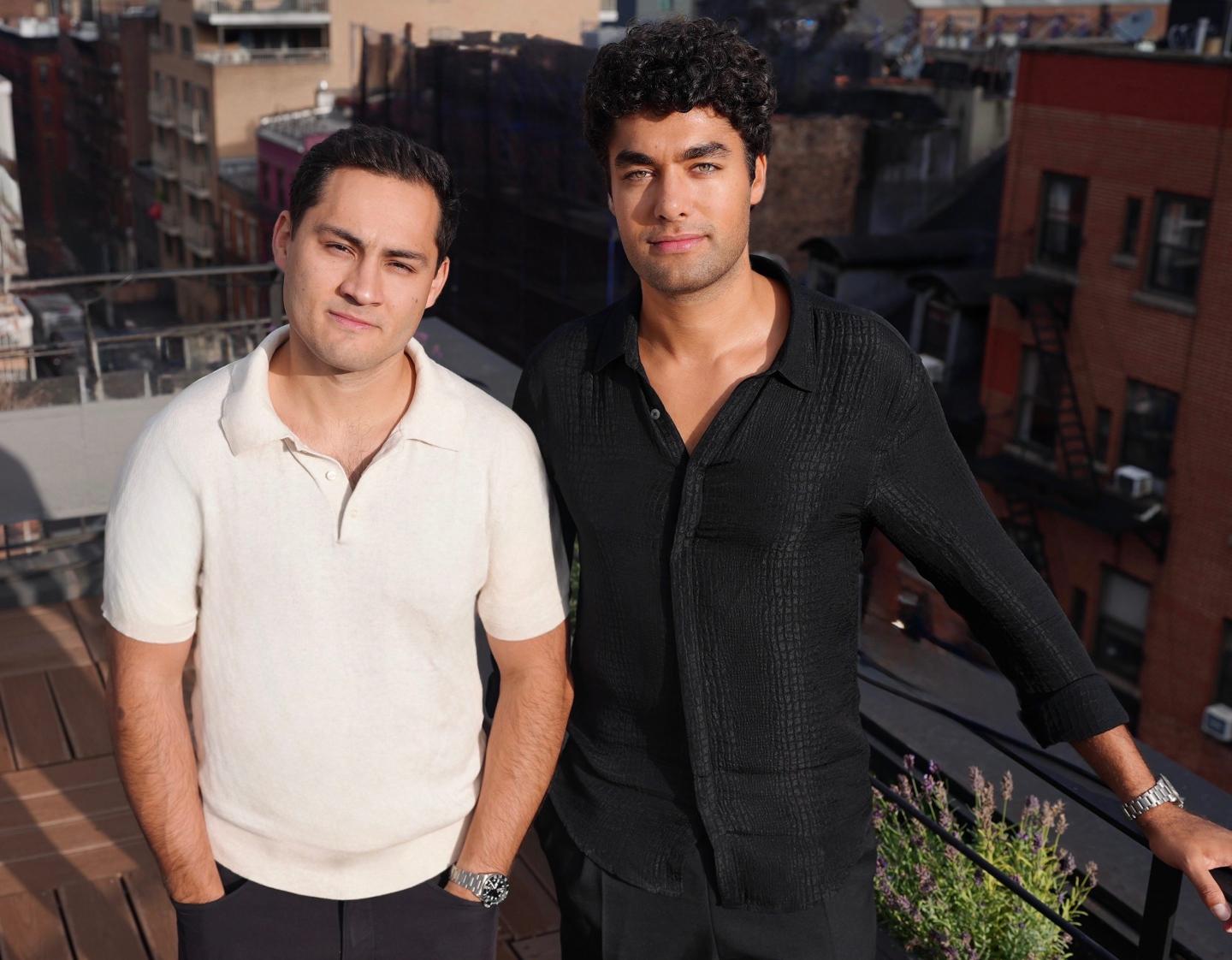 Chris Fernandes (left) and Sinclair Toffa (right) stand next to each other and faintly smile at the camera from a terrace in NYC.